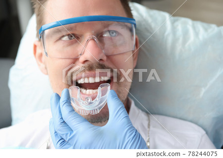 Dentist trying on mouthguard for man patient 78244075