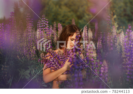 woman brunette with bouquet of flowers in lupine field sits in grass and enjoys sun woman brunette with bouquet of flowers in lupine field sits in grass and enjoys sun 78244113