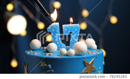 Birthday cake number 17 stars sky and moon concept, blue candle is fire by lighter. Copy space on right side of screen. Close-up 78245263