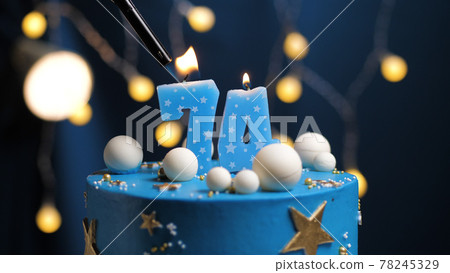 Birthday cake number 74 stars sky and moon concept, blue candle is fire by lighter. Copy space on right side of screen. Close-up 78245329