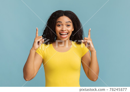 Look upward. Overjoyed african american woman pointing fingers up, looking and smiling to camera on blue background 78245877