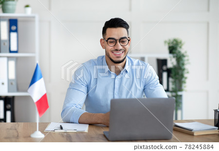 Online foreign languages tutoring. Cheerful Arab male teacher giving French class, communicating on laptop from home 78245884