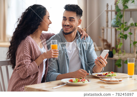 Happy Young Arab Couple Using Smartphone During Breakfast In Kitchen 78245897