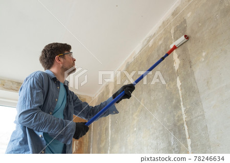 Caucasian man painting cement walls using roller brush and primer making a renovation. Caucasian man painting cement walls using roller brush and primer making a renovation. 78246634