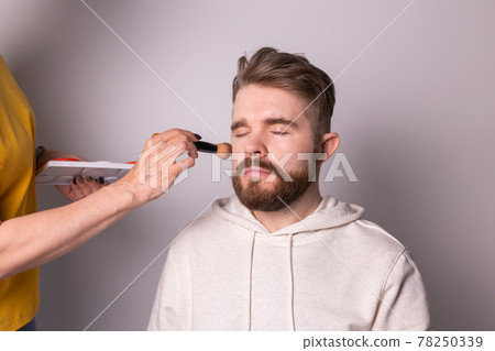 Professional make-up artist doing young man makeup in studio 78250339