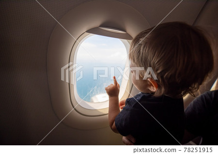 resumption of flights, opening of borders concept. a small child looks at the ocean from the window of a flying plane. the first flight. vacation happiness 78251915