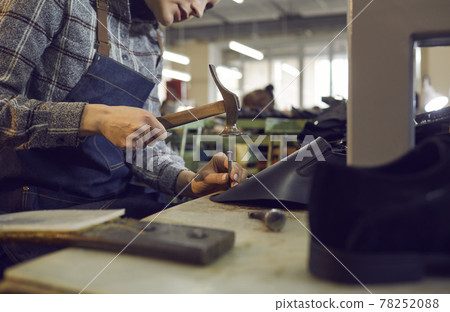 Shoe factory worker sitting at table and using professional tools to make leather boots 78252088