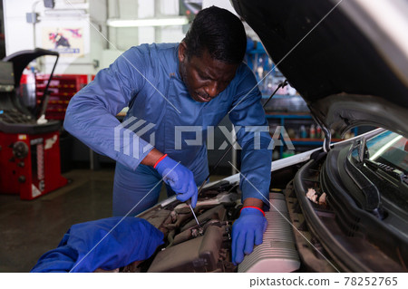 Professional american mechanic man in uniform repairing car engine 78252765