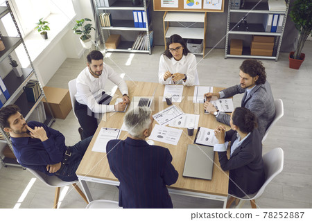 Team of young workers listening to senior manager sitting around office table in corporate meeting Team of young workers listening to senior manager sitting around office table in corporate meeting 78252887