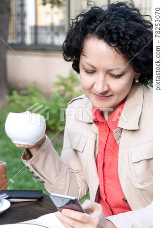 woman with a mobile phone communicates online while sitting in a cafe over a cup of coffee woman with a mobile phone communicates online while sitting in a cafe over a cup of coffee 78253070
