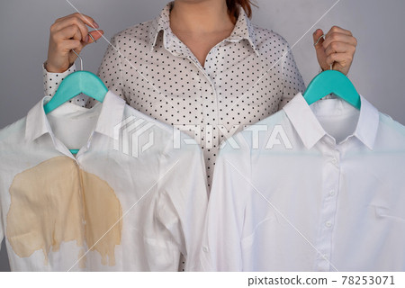A woman compares two white shirts before and after washing. The girl is holding one blouse, clean and ironed, and the other, dirty with coffee stains A woman compares two white shirts before and after washing. The girl is holding one blouse, clean and ironed, and the other, dirty with coffee stains 78253071