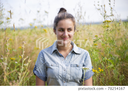 beautiful young woman sits in a meadow in flowers on a sunny summer day and smiles. beautiful young woman sits in a meadow in flowers on a sunny summer day and smiles. 78254167