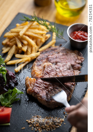 cutting steak with knife and fork on black plate 78254381