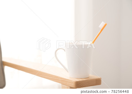 窗邊沙發扶手上放著一個帶牙刷的杯子 窗邊沙發扶手上放著一個帶牙刷的杯子 78256448