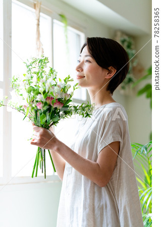 Woman looking at a bouquet by the window 78258365