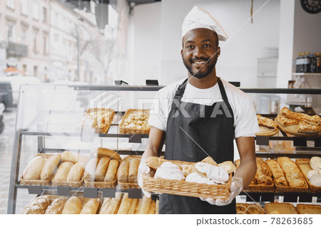 African American baker holding tray of bread in bakery 78263685