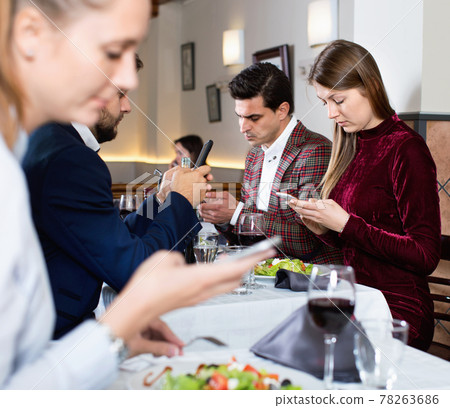 Modern young people busying with phone during evening meal at restaurant 78263686
