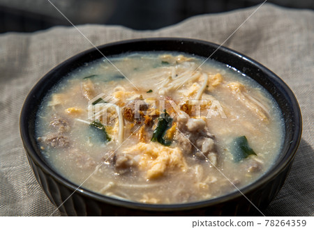 Close-up of Pork congee or Chinese rice porridge with Minced pork, Egg, Enoki mushroom and Seaweed in bowl on white placemat. Asian breakfast, Selective focuse. Close-up of Pork congee or Chinese rice porridge with Minced pork, Egg, Enoki mushroom and Seaweed in bowl on white placemat. Asian breakfast, Selective focuse. 78264359