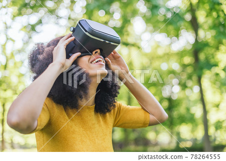 Afro woman wearing a virtual reality glasses in a garden. 78264555