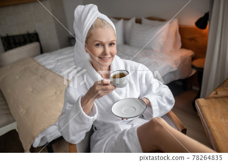 Beautiful woman in a white robe having coffee after the bath Beautiful woman in a white robe having coffee after the bath 78264835