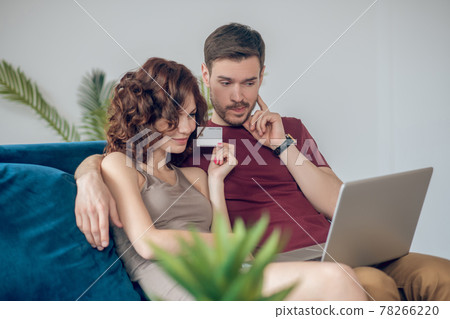 A man and a woman sitting on the sofa with a laptop 78266220