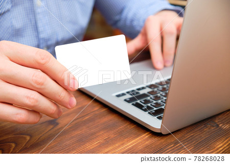 A man sits in a shirt at a laptop and shows a card with mock and copy space. A man sits in a shirt at a laptop and shows a card with mock and copy space. 78268028