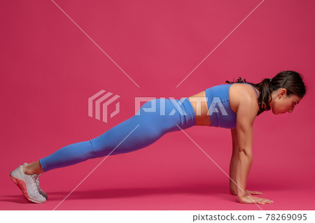 Girl performing front plank on straight arms on maroon background Girl performing front plank on straight arms on maroon background 78269095