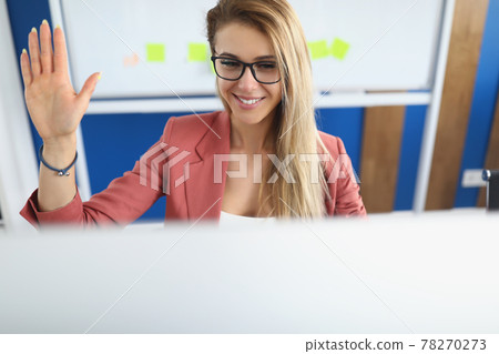 Young woman waving hand at computer screen in office 78270273