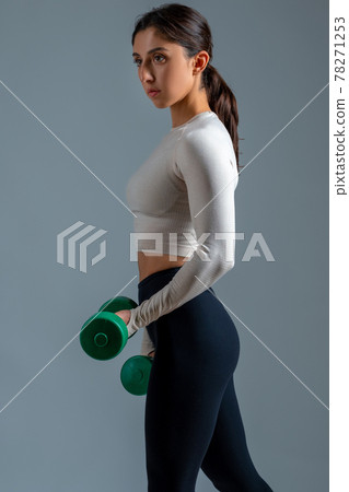 Girl performing arm exercises with dumbbells on grey background Girl performing arm exercises with dumbbells on grey background 78271253