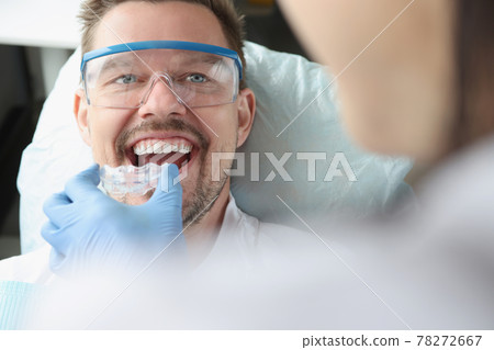 Doctor tries on plastic mouthguard for young smiling man to correct bite Doctor tries on plastic mouthguard for young smiling man to correct bite 78272667