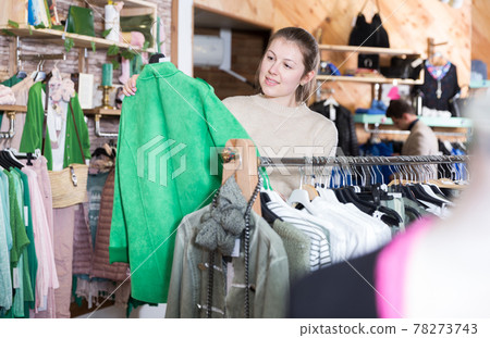 Young female is looking on green jacket and choosing Young female is looking on green jacket and choosing 78273743