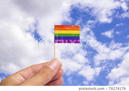 Small LGBT flag in hand on blue sky background Small LGBT flag in hand on blue sky background 78274276