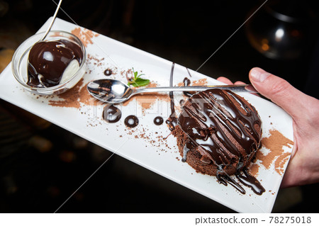 The waiter holds in his hand a classic chocolate fondant with ice cream. Close-up, selective focus 78275018
