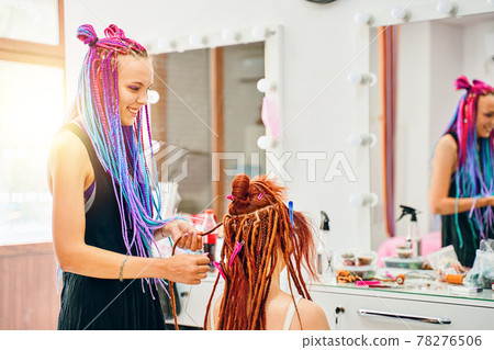 Woman hairdresser weaves to girl ginger dreadlocks. 78276506