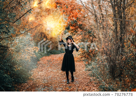 Girl dressed as witch casts fire spell in front of the forest Girl dressed as witch casts fire spell in front of the forest 78276778