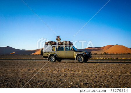 A photographer on top of a 4x4 in the desert of sossusvlei, namibia. 78279214