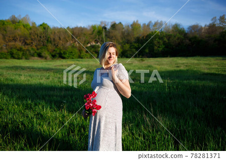 pregnant woman on a green meadow walking with a bouquet of flowers 78281371