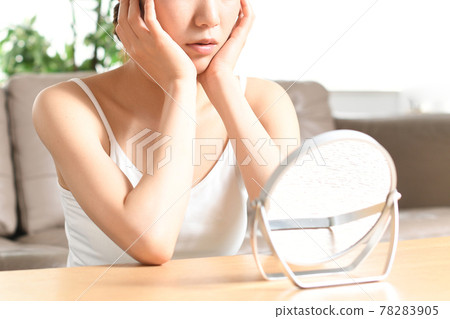 A woman suffering from skin problems while looking in the mirror 78283905