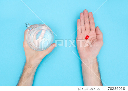 The man is holding a red pill and a glass of water. Blue background. Medical background. Taking Medication. 78286038