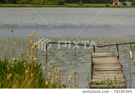 Old rustic pier on the shore of the lake in a cloudy noon. Old rustic pier on the shore of the lake in a cloudy noon. 78286369