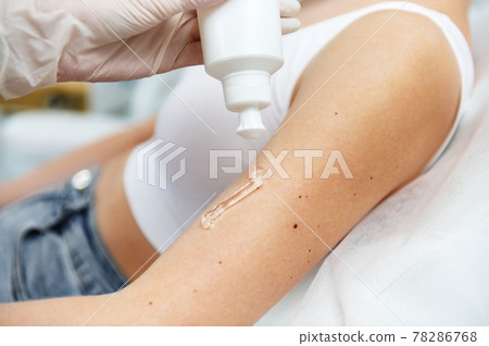 Close-up shot of squeezed transparent anesthetic gel for laser epilation procedure from a white container on female hand in spa salon 78286768