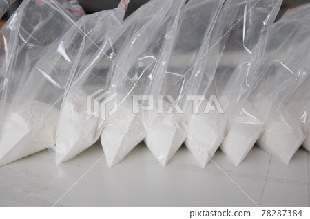 A large number of transparent sachets filled with white powder. White powder packaged in small sachets. 78287384