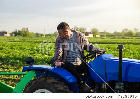 A farmer on a tractor monitors the operation of equipment for harvesting potatoes. Farming and farmland. Simplify speed up work with technology and machines. Agro industry and agribusiness A farmer on a tractor monitors the operation of equipment for harvesting potatoes. Farming and farmland. Simplify speed up work with technology and machines. Agro industry and agribusiness 78289989