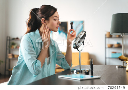 Young pretty woman does makeup at home while looking in the mirror Young pretty woman does makeup at home while looking in the mirror 78291549