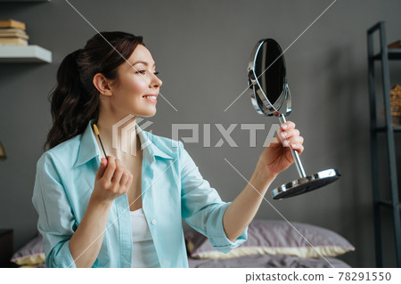 Young pretty woman does makeup at home while looking in the mirror Young pretty woman does makeup at home while looking in the mirror 78291550