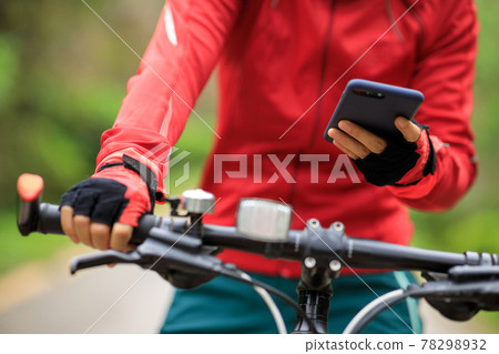 Cyclist use smartphone when riding mountain bike on forest trail Cyclist use smartphone when riding mountain bike on forest trail 78298932