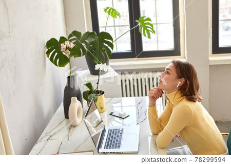 Woman sitting at table with laptop and listening to music 78299594