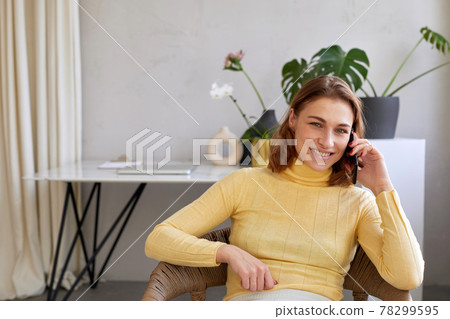 Female freelancer speaking on smartphone in light workspace 78299595