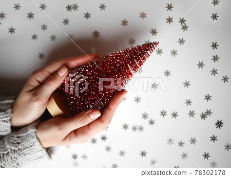 beautiful female hands holding a small red christmas tree on a gray background. View from above 78302178