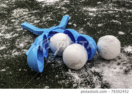 snowball maker is lying on the asphalt next to three snowballs 78302452